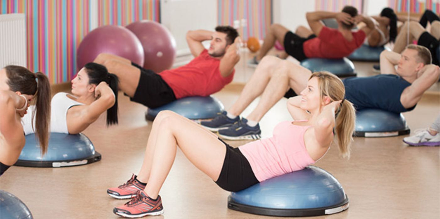 Gruppe jüngerer Menschen bei Situps im Fitness-Studio auf halbem Gymnastikball