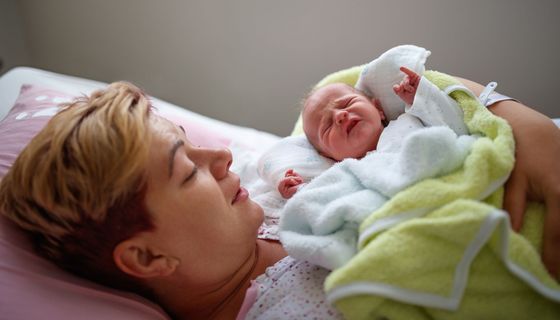 Junge Frau mit Neugeborenem im Arm.
