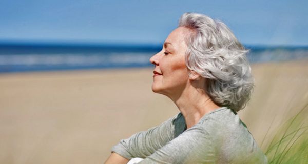 Ältere grauhaarige Frau im Profil zu sehen sitzt am Meer und genießt die Seeluft