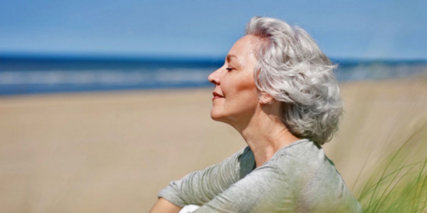 Ältere Frau sitzt am Strand.