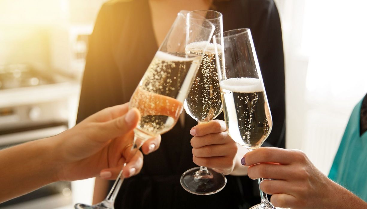 Drei Frauen stoßen mit einem Glas Sekt an.