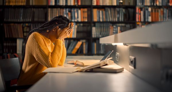 Frau, sitzt in der Bibliothek am Abend und stützt den Kopf in die Hände.