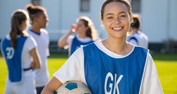 Junges Mädchen mit Fußball, lächelt in die Kamera.