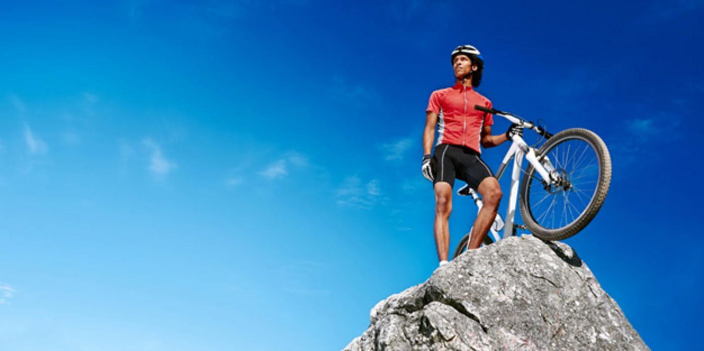Sportiver attraktiver Rennradfahrer mit Fahrrad auf einem Berggipfel, ins Weite blickend