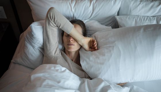 Frau, liegt im Bett und hat Kopfschmerzen.