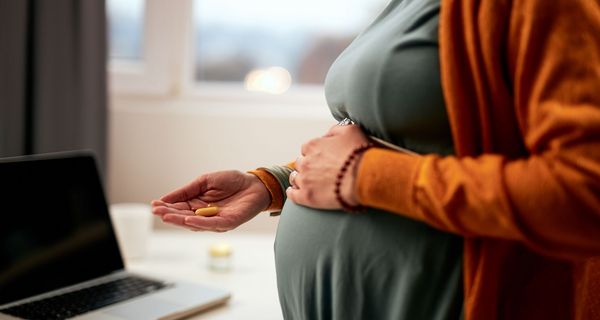Schwangere Frau hält Nahrungsergänzungsmittel in der Hand.