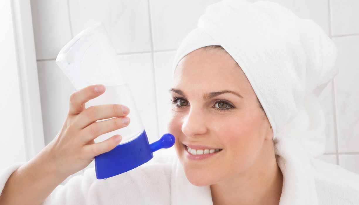 Frau mit Handtuchturban nutzt Nasendusche.