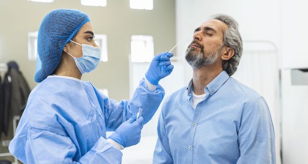 Frau mit Schutzkleidung, macht einen Corona-Test bei einem älteren Mann.