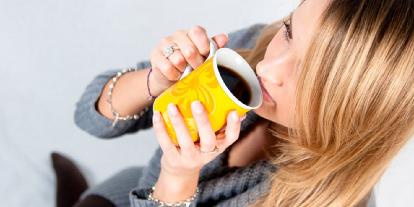 Frau trinkt Kaffee aus gelber Tasse.
