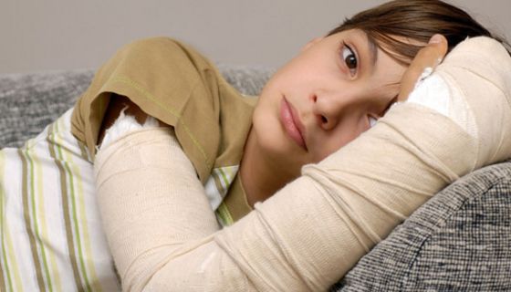 Nahaufnahme: dunkelhaariges Kind, ca. 12 Jahre, auf Couch liegend, traurig schauend, rechter Arm eingegipst
