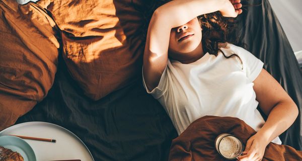 Frau, liegt im Bett mit einer Tasse Kaffee.