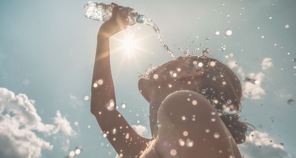 Frau, schüttet sich an einem sonnigen Tag Wasser über ihr Gesicht.