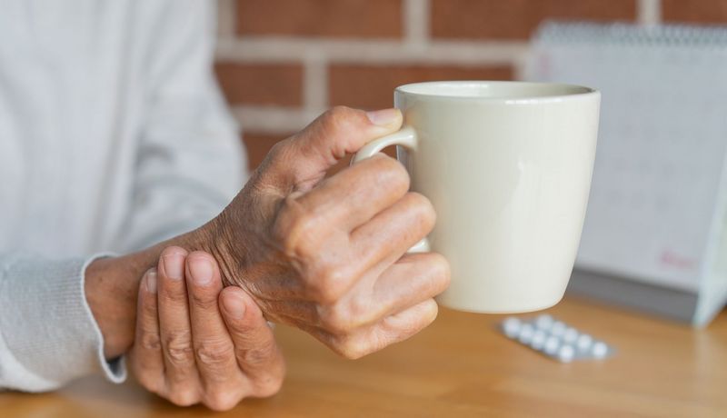 Eine ältere Person hält eine Tasse und stützt ihr Handgelenk mit der anderen Hand ab.