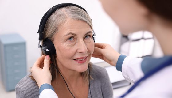 Frau, bekommt beim Arzt Kopfhörer angezogen.