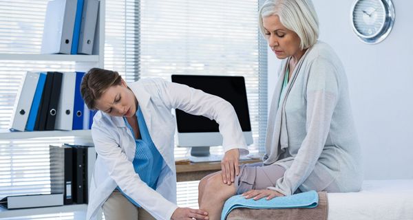 Ärztin untersucht das Knie einer Seniorin.