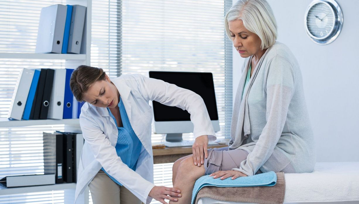 Ärztin untersucht das Knie einer Seniorin.