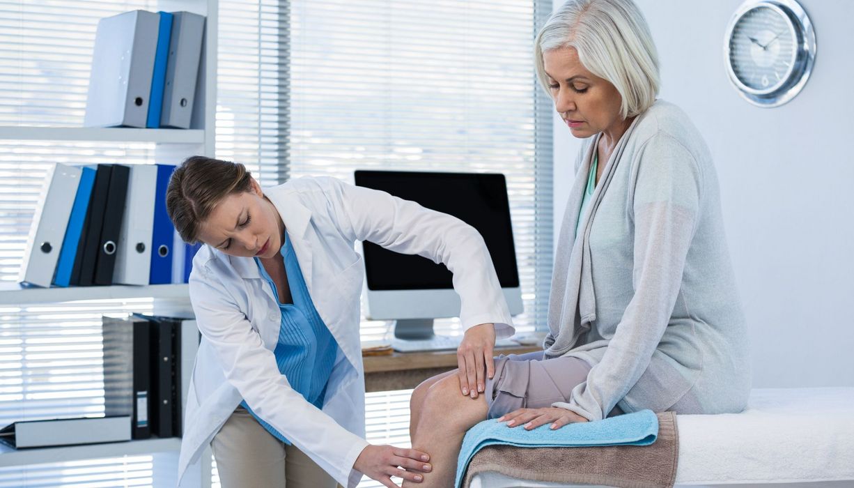Ärztin untersucht das Knie einer Seniorin.