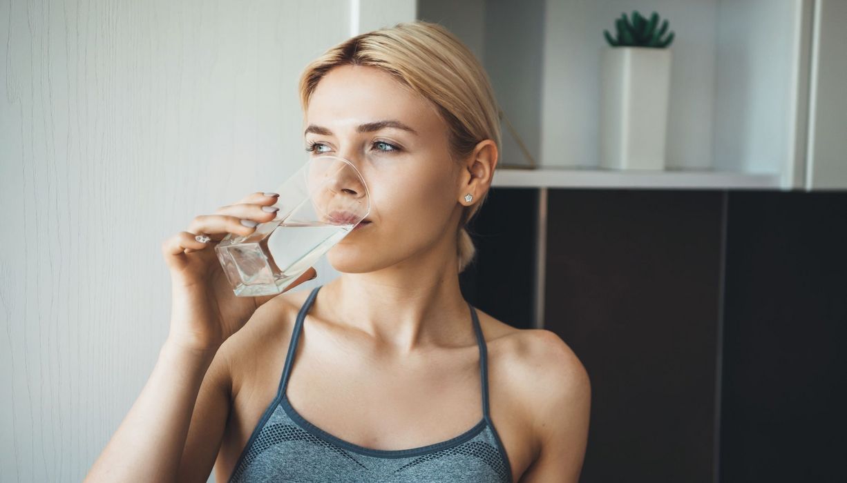 Junge blonde Frau, trinkt ein Glas Wasser.