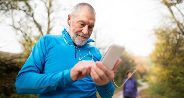 Älterer Mann, in Sportkleidung draußen, schaut auf sein Smartphone.
