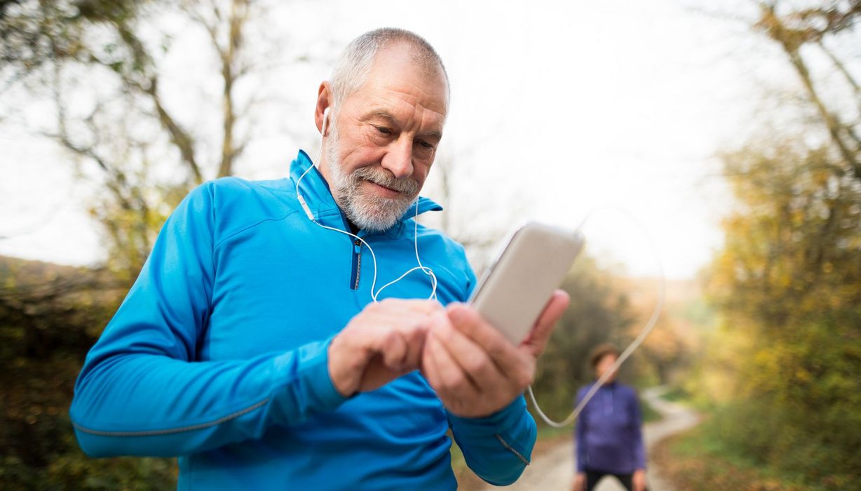 Älterer Mann, in Sportkleidung draußen, schaut auf sein Smartphone.