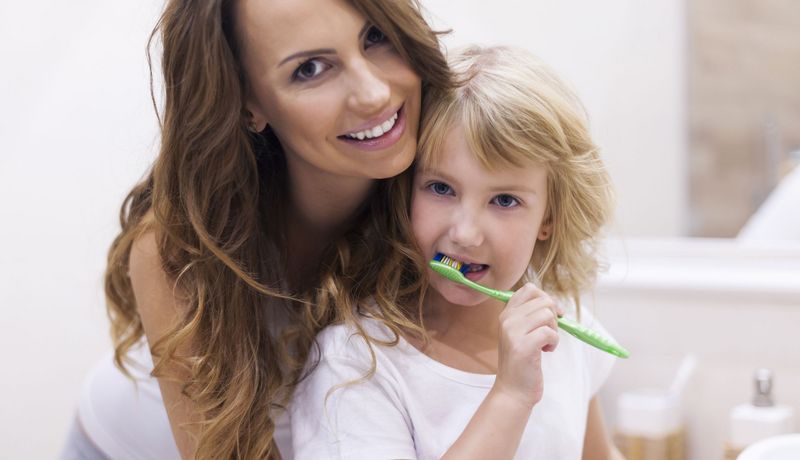 Mutter steht mit kleinem Mädchen vor dem Badezimmerspiegel und das Kind putzt sich die Zähne.