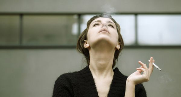 Frontalfoto Frau in der Bildmitte schaut nach oben und bläst Rauch in die Luft