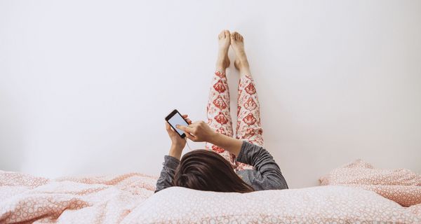 Junges Mädchen, liegt mit Smartphone im Bett.