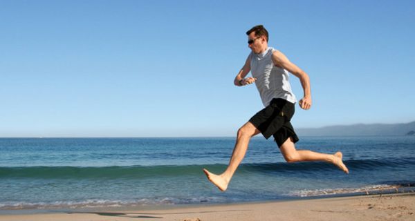 Mann läuft barfuß am Strand.