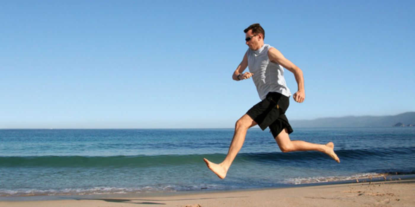 Mann läuft barfuß am Strand.