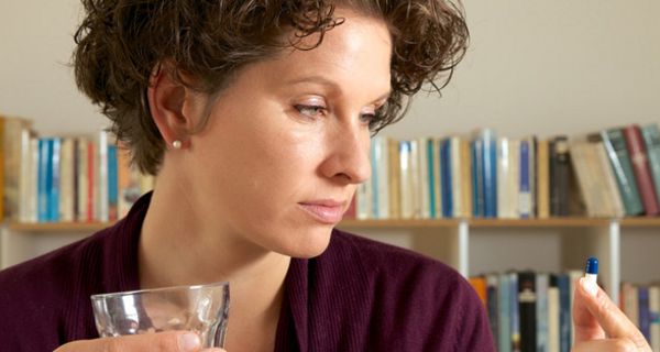 Frau schaut skeptisch auf Kapsel, die sie gerade mit einem Glas Wasser einnehmen will