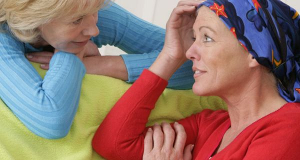 Brustkrebspatientin ca. Mitte, Ende 40, blaugemustertes Kopftuch, roter Pulli, im Gespräch mit blonder Frau um die 50, blond, helllauer Pulli