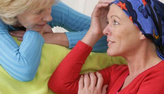 Brustkrebspatientin ca. Mitte, Ende 40, blaugemustertes Kopftuch, roter Pulli, im Gespräch mit blonder Frau um die 50, blond, helllauer Pulli