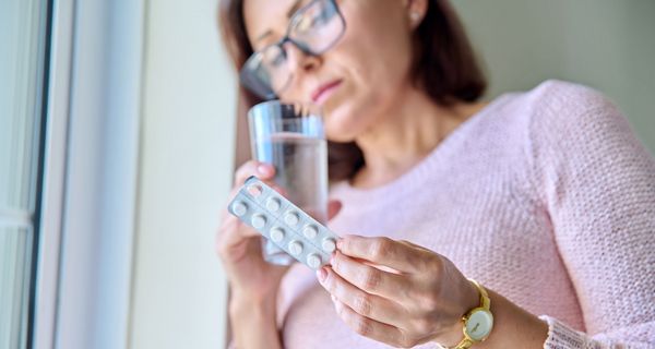 Frau, schaut skeptisch auf einen Blister mit Tabletten.