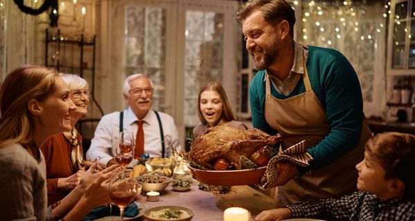 Eine Familie sitzt um den Weihnachtstisch herum. Ein Mann serviert eine große Gans