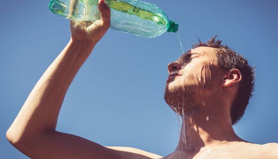 Mann mit freiem Oberkörper lässt sich Wasser über das Gesicht laufen.