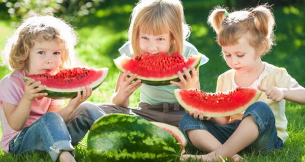 Drei Mädchen sitzen auf einer Wiese und essen Wassermelone