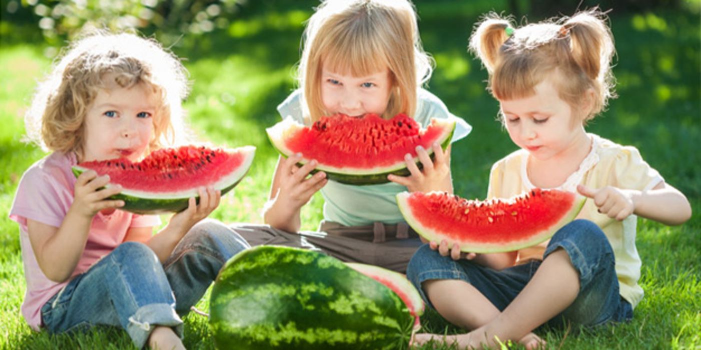 Drei Mädchen sitzen auf einer Wiese und essen Wassermelone