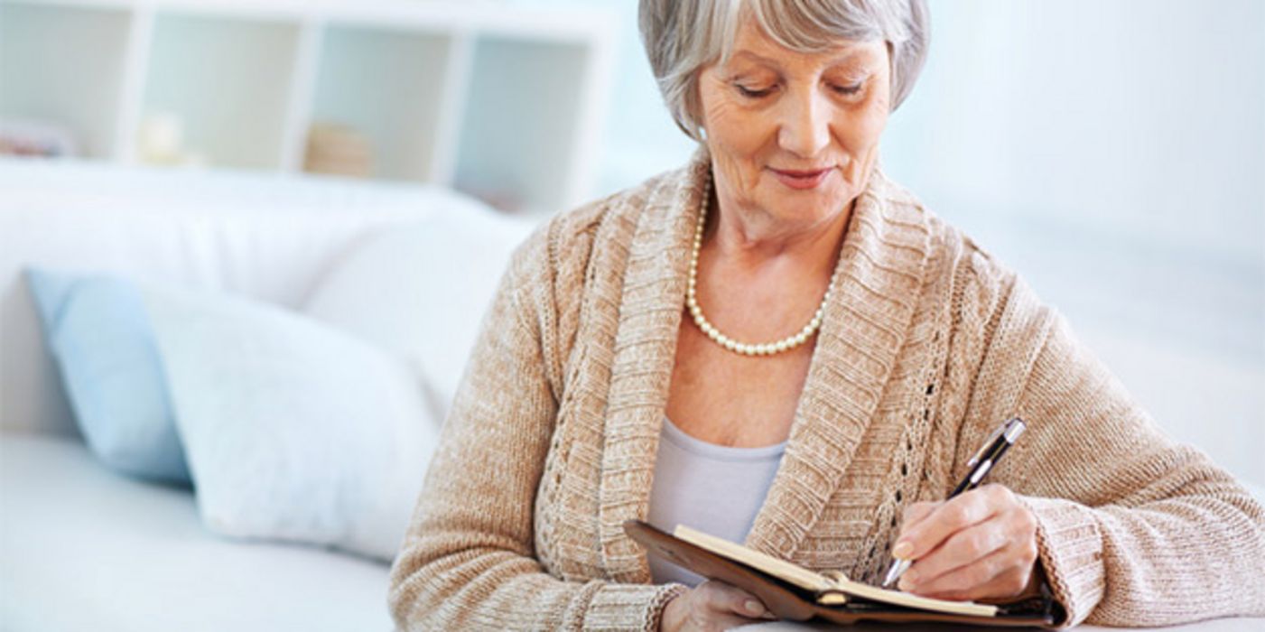 Frau in den 60ern, grauhaarig, lächelnd, schreibt in Tagebuch