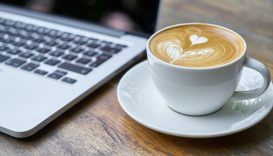 Tasse Kaffee neben Laptop.