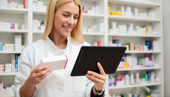 Apothekerin, hält ein Medikament und ein Tablet in der Hand.