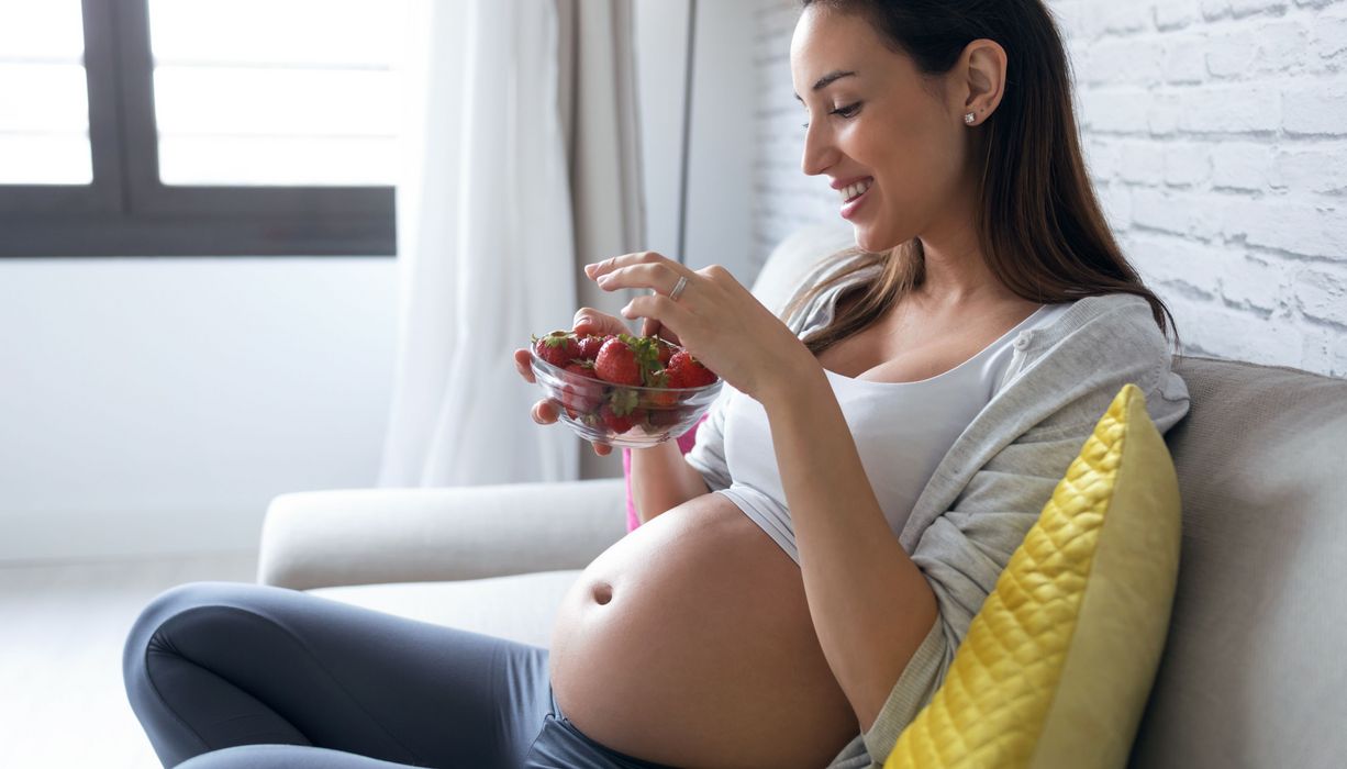 Schwangere Frau isst Erdbeeren.