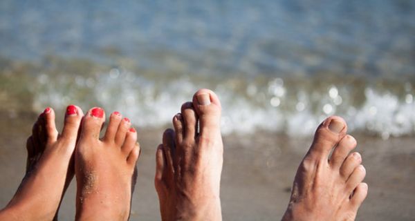 Je ein Paar Frauen- und Männerfüße strecken sich am unteren Bildrand ins Bild, dahinter Strand und Meer