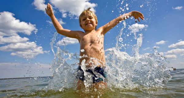 Junge steht im knietiefen Wasser im Meer und spritzt mit dem Wasser