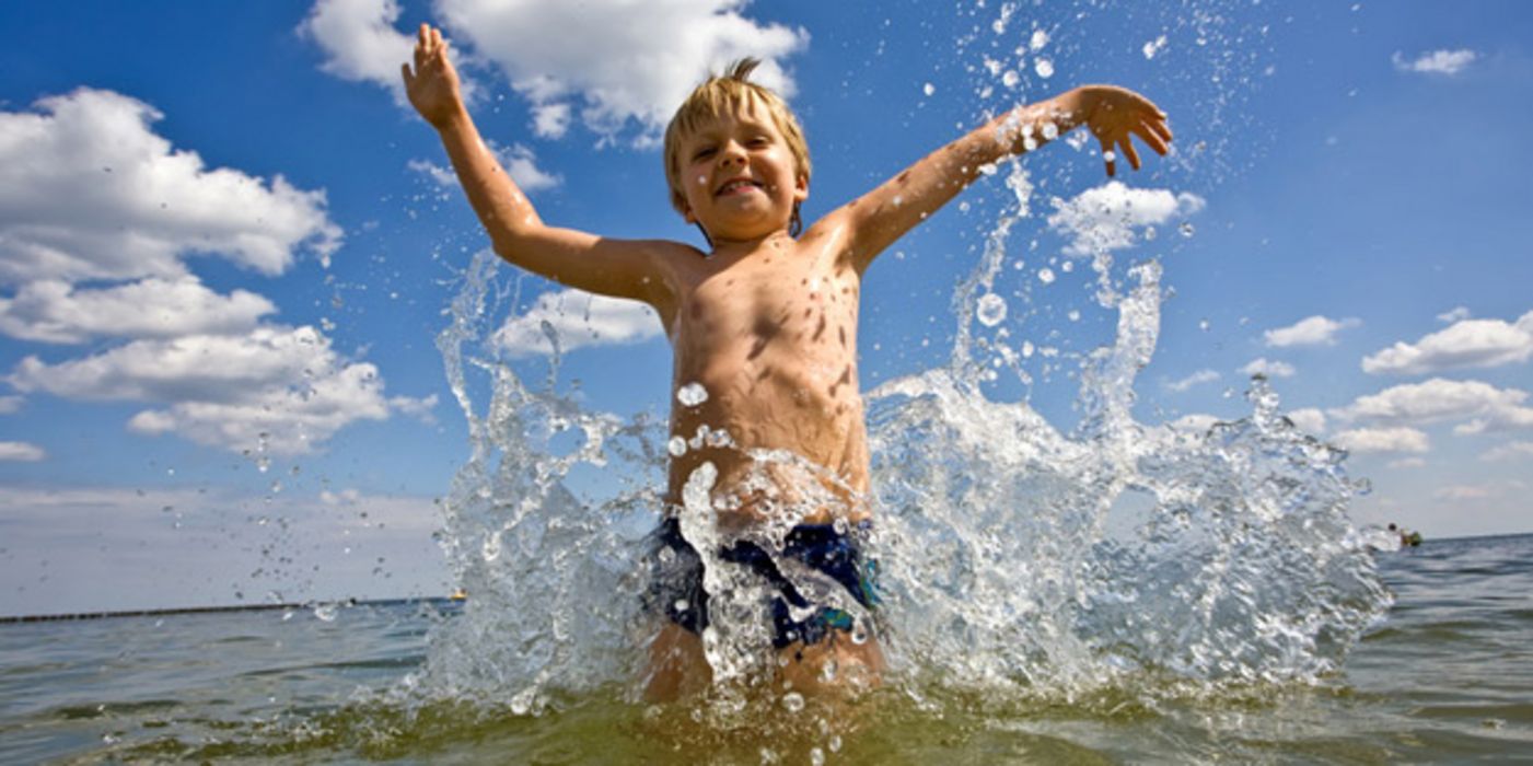 Junge steht im knietiefen Wasser im Meer und spritzt mit dem Wasser