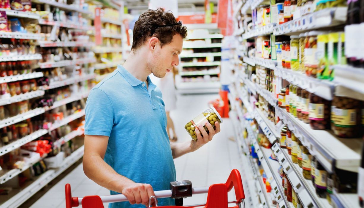 Junger Mann im Supermarkt, betrachtet das Etikett eines Lebensmittels.