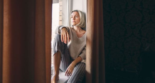 Frau, sitzt auf der Fensterbank und schaut traurig nach draußen.