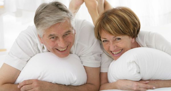 Vitales Seniorenpaar liegt bäuchlings im Bett und lacht in die Kamera