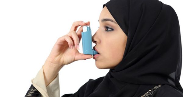 Junge Muslimin mit schwarzem Kopftuch inhaliert Asthmaspray.