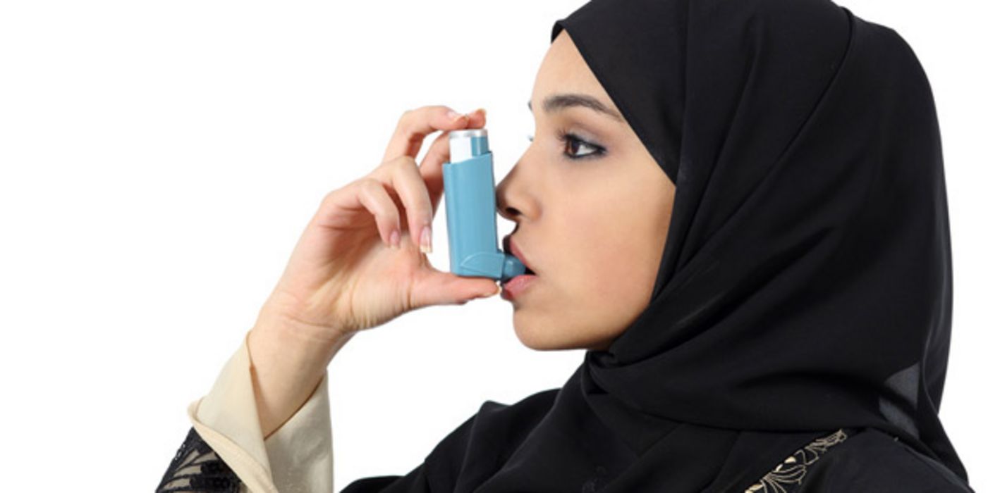 Junge Muslimin mit schwarzem Kopftuch inhaliert Asthmaspray.