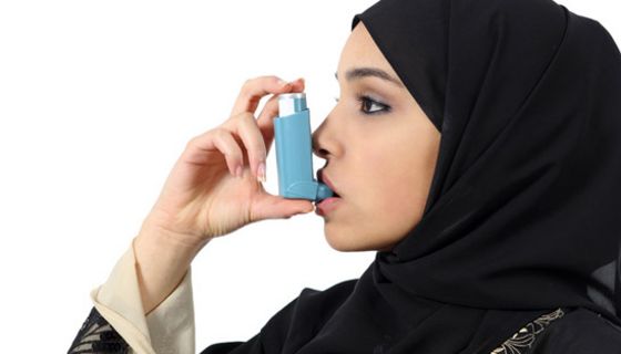 Junge Muslimin mit schwarzem Kopftuch inhaliert Asthmaspray.
